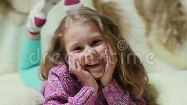 美丽的小女孩对着镜头微笑。 躺在沙发上的快乐孩子的肖像
